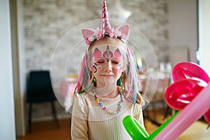 Little preschooler girl in unicorn costume with facepaint on a birthday party