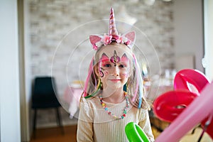 Little preschooler girl in unicorn costume with facepaint on a birthday party