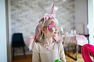 Little preschooler girl in unicorn costume with facepaint on a birthday party