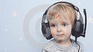 A little pretty child listening music in headphones. A boy in headphones on blue background