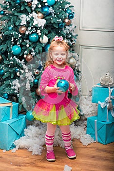 Little pretty curly blonde smiling girl standing nearly Christmas tree