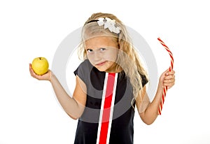 Little pretty female child choosing dessert holding unhealthy but tasty red candy licorice and apple fruit