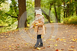 Little pretty girl in a beige coat, autumn in the park collects