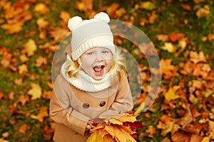 Little pretty girl in a beige coat laughs in a park in autumn, c