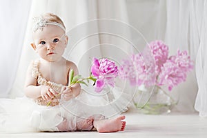 Little pretty girl with blue eyes sits on a floor with flowers of a peony. Copy space