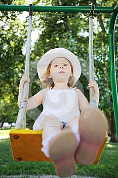 Little pretty girl in hat sits on swing at