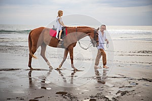 Little pretty girl on a horse. Father leading horse by its reins on the beach. Horse riding by the sea. Family concept. Father`s