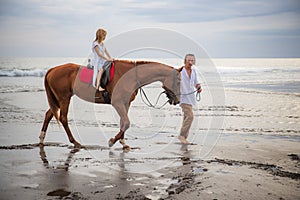 Little pretty girl on a horse. Father leading horse by its reins on the beach. Horse riding by the sea. Family concept. Father`s