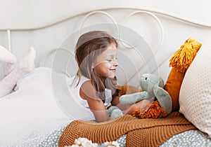 Little pretty girl plays on the bed in the sleeper with a soft toy