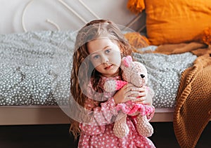Little pretty girl plays with soft toy bear in children`s bedroom
