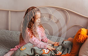 A little pretty girl plays with toys on her bed in the children`s room