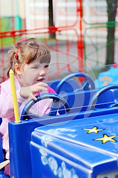 Little pretty girl rides on bright car in amusement park