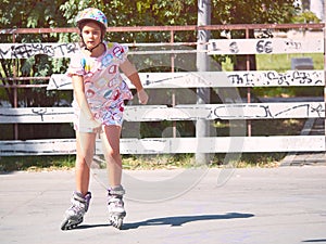 Little pretty girl on roller skates in helmet at a park