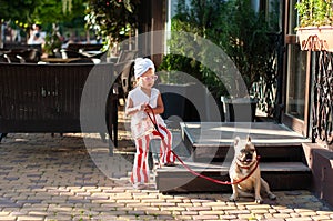 Little pretty girl stylishly dressed holding her French bulldog dog on a leash