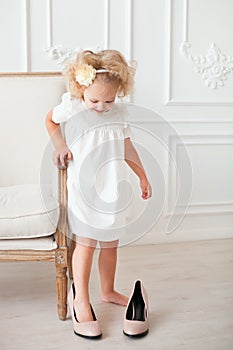 Little pretty girl in white dress trying on mummy's shoes