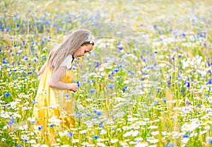 Little pretty girl in yellow Russian dress picking flowers in field of wild flowers on summer day