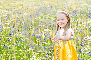 Little pretty girl in yellow Russian dress picking flowers in field of wild flowers on summer day