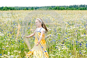 Little pretty girl in yellow Russian dress picking flowers in field of wild flowers on summer day