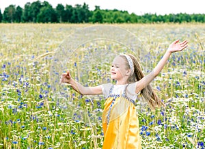 Little pretty girl in yellow Russian dress picking flowers in field of wild flowers on summer day