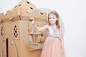 Little princess in crown play with her cardboard castle. True emotion of happiness of the child.