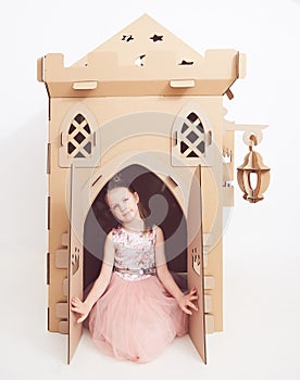 Little princess in crown play with her cardboard castle. True emotion of happiness of the child.