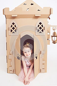 Little princess in crown play with her cardboard castle. True emotion of happiness of the child.