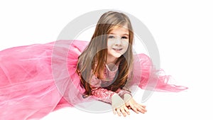 Little Princess. Portrait of a cute Caucasian little laughing girl in an evening bright pink dress lies on a white background.