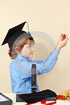 Little professor in academic hat conducts scientific research with microscope