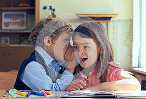 Little pupils whispering secrets during class at the elementary school.