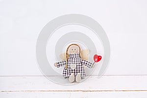 Little puppet with a red heart sitting on a wooden white background