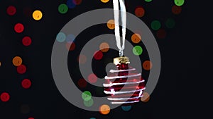 Little red Christmas ornament with glitter swing with blinking lights behind
