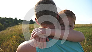 Little red-haired boy sitting on green grass on the lawn with his father and hugging him with love. Happy son embracing