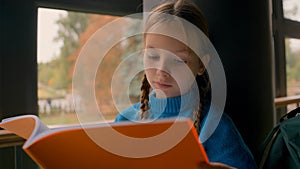 Little red-haired European girl sitting reading notebook studying school homework knowledge looking window pupil prepare