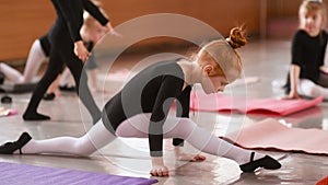 Little red-haired girl ballerina stretching and doing exercises in ballet school