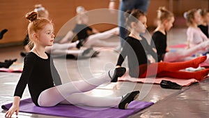 Little red-haired girl ballerina stretching and doing exercises in ballet school