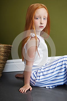 Little red-haired girl with a basket of flowers posing on an olive background. Spring portrait of a redhead girl with blue eyes.
