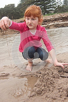 Little red haired girl building a sand castle with wet sand at a