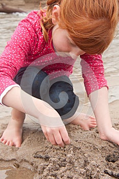 Little red haired girl building a sand castle with wet sand at a