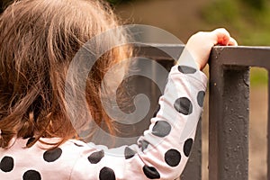 Little red-haired girl holding a turnstile in a summer park