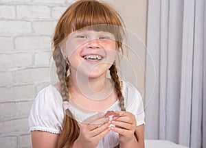 Little red-haired girl in a white dress holds a plate in her hands to correct a bite of teeth