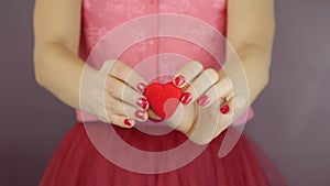 Little red heart in female hands, close up. Woman holds red heart gift for St. Valentine`s Day. Concept of love. Female is showing