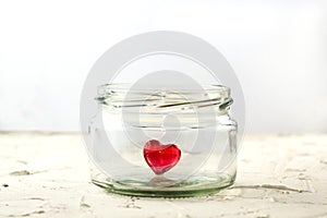 Little red heart in glass jar on white background