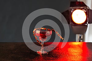 Little red snake with language in a glass with red liquid against the background of a searchlight and a dark background