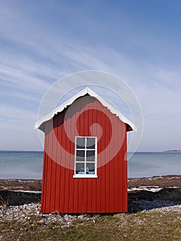 A little red wooden beach hut with blue sea and a windswept blue sky, Aero, Denmark