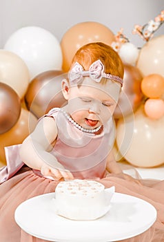 Little redhead baby girl celebrates first birthday. Cake crash smash, hands eating. 1 year family baloons party