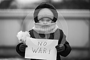Little refugee girl with a sad look and a poster that says no to war. Social problem of refugees and internally displaced persons