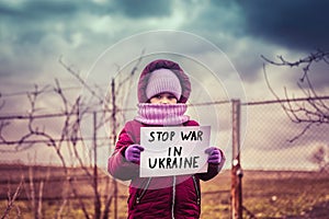 Little refugee girl with a sad look and a poster that says stop war in Ukraine. Social problem of refugees and internally displace