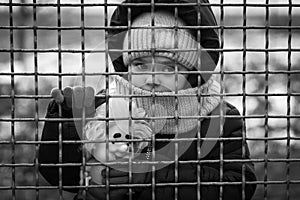 Little refugee girl with a toy behind a metal fence. Social problem of refugees and internally displaced persons. Russia`s war