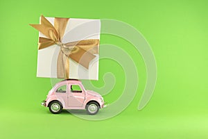 Little retro toy model car with present gift box on light green background. Christmas, birthday, valentines day