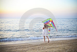 Little running girl with flying kite on beach at sunset